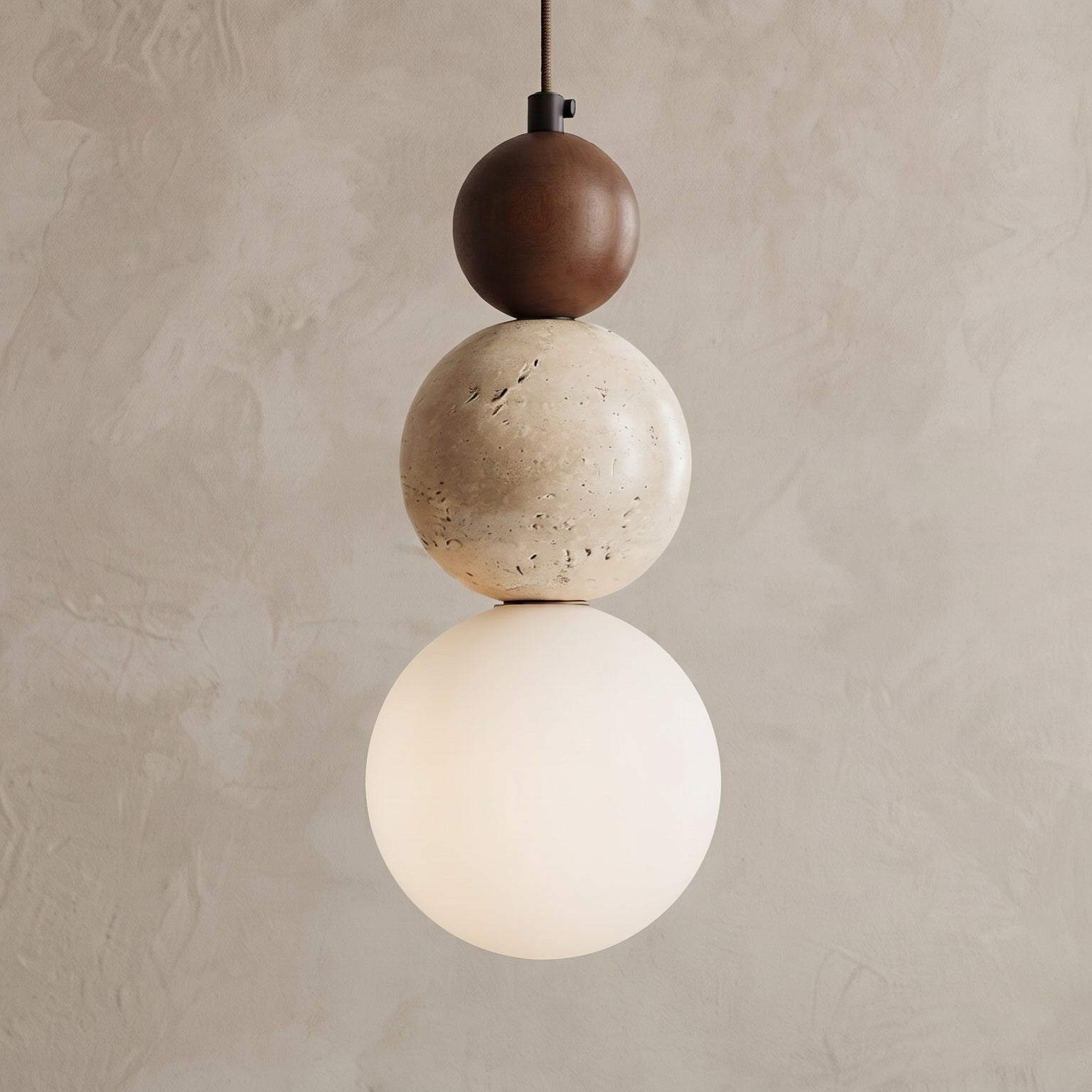 A modern three-sphere pendant light hanging against a textured beige plaster wall. The light features a dark brown top sphere, a speckled cream middle sphere, and a glowing warm white bottom globe shade.