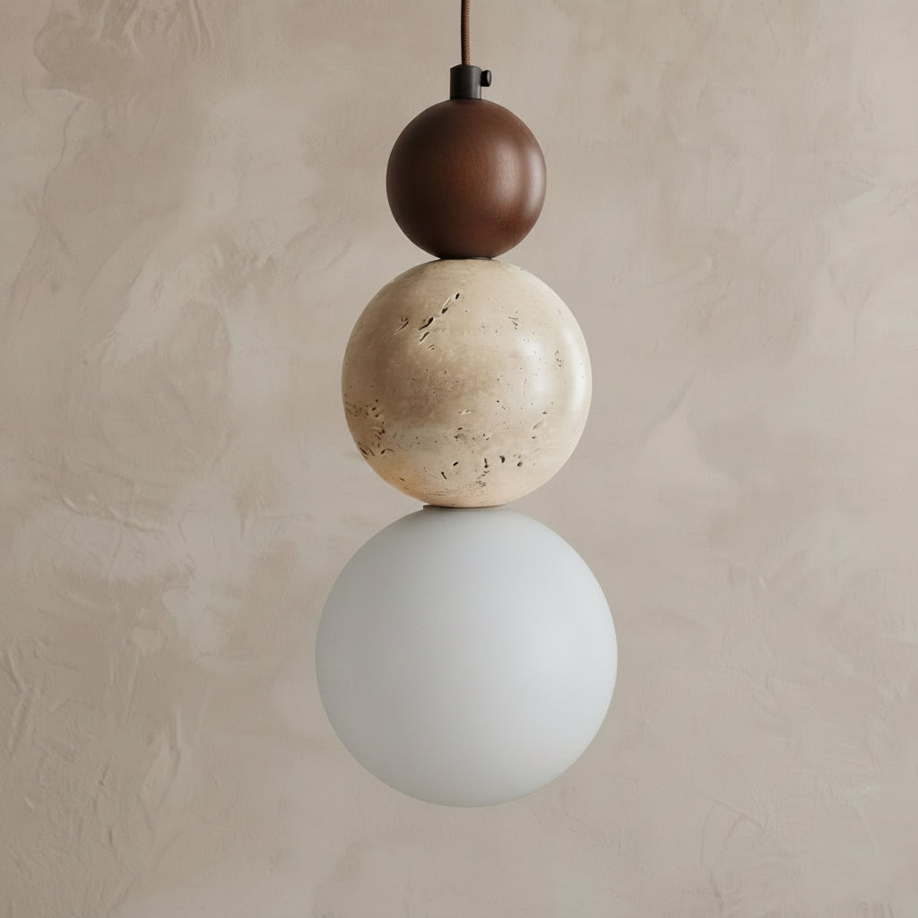 A modern three-sphere pendant light hanging against a textured beige plaster wall. The light features a dark brown matte sphere on top, a natural beige travertine stone sphere in the middle, and a frosted white glass sphere on the bottom.