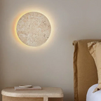Round wall light fixture on a neutral wall next to a bed with beige headboard and pillows.