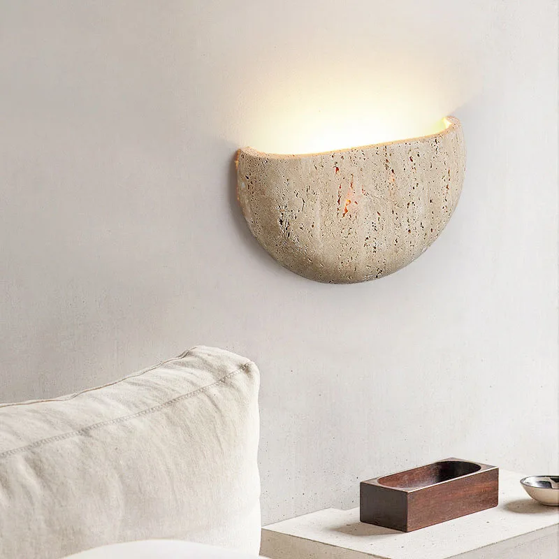 Concrete wall sconce on a neutral wall with a pillow and small wooden box in the foreground.