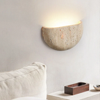 Concrete wall sconce on a neutral wall with a pillow and small wooden box in the foreground.