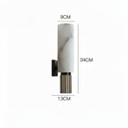 A wall-mounted light fixture shown with dimension labels: 9CM width at the top, 34CM height, and 13CM width at the bottom. The fixture has a white marble cylinder, a black wall mount, and a fluted lower section with vertical metallic stripes.
