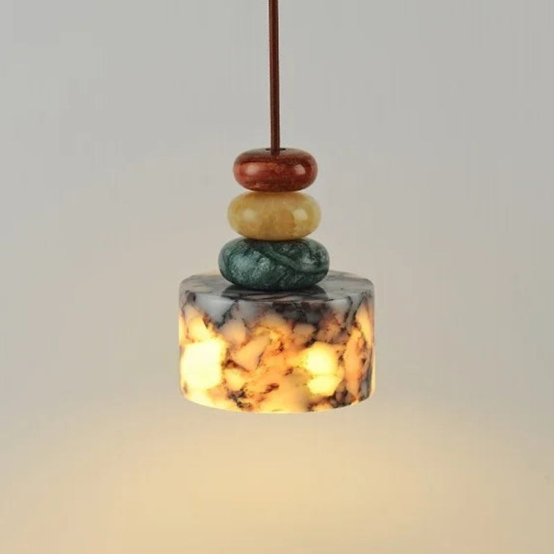 Decorative pendant light with stacked stones above a book and cup on a neutral background