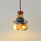 Decorative pendant light with stacked stones above a book and cup on a neutral background