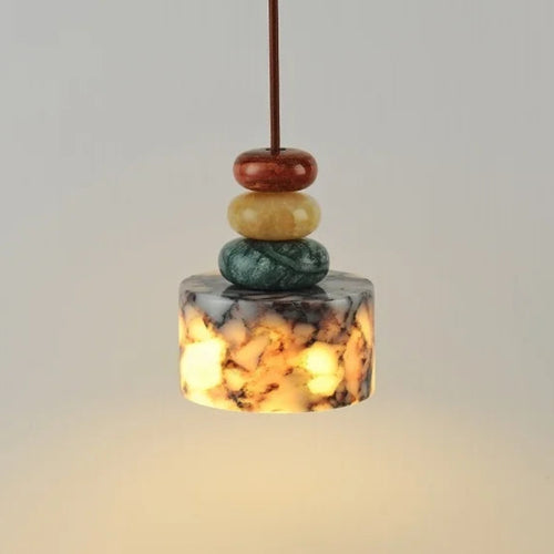 Decorative pendant light with stacked stones above a book and cup on a neutral background