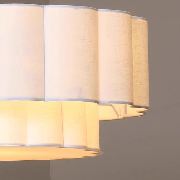A close-up of a modern pleated fabric ceiling light fixture glowing with warm yellow light against a neutral gray background.