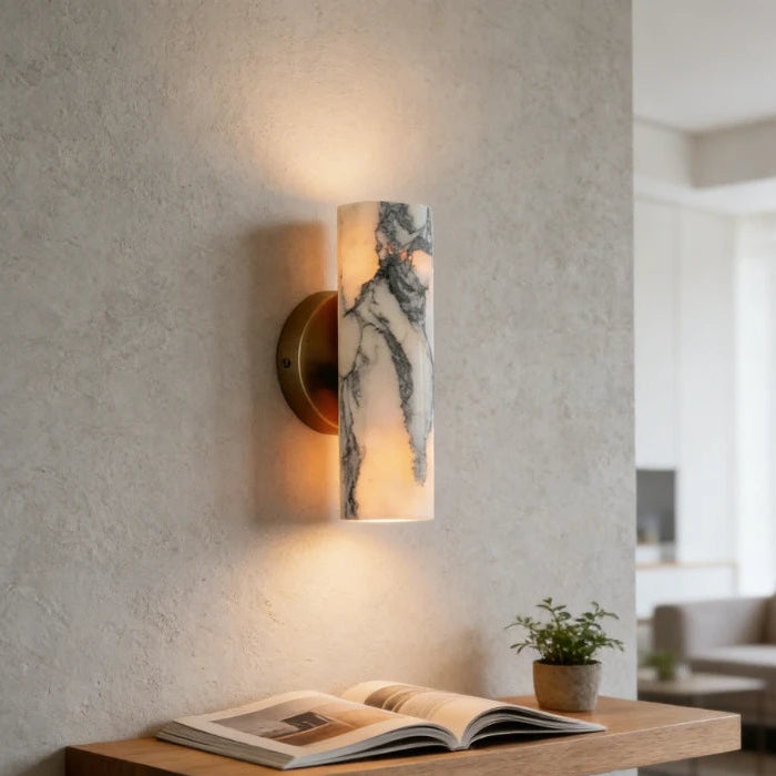 Modern wall sconce with a textured finish on a neutral wall, next to an open book on a wooden shelf.