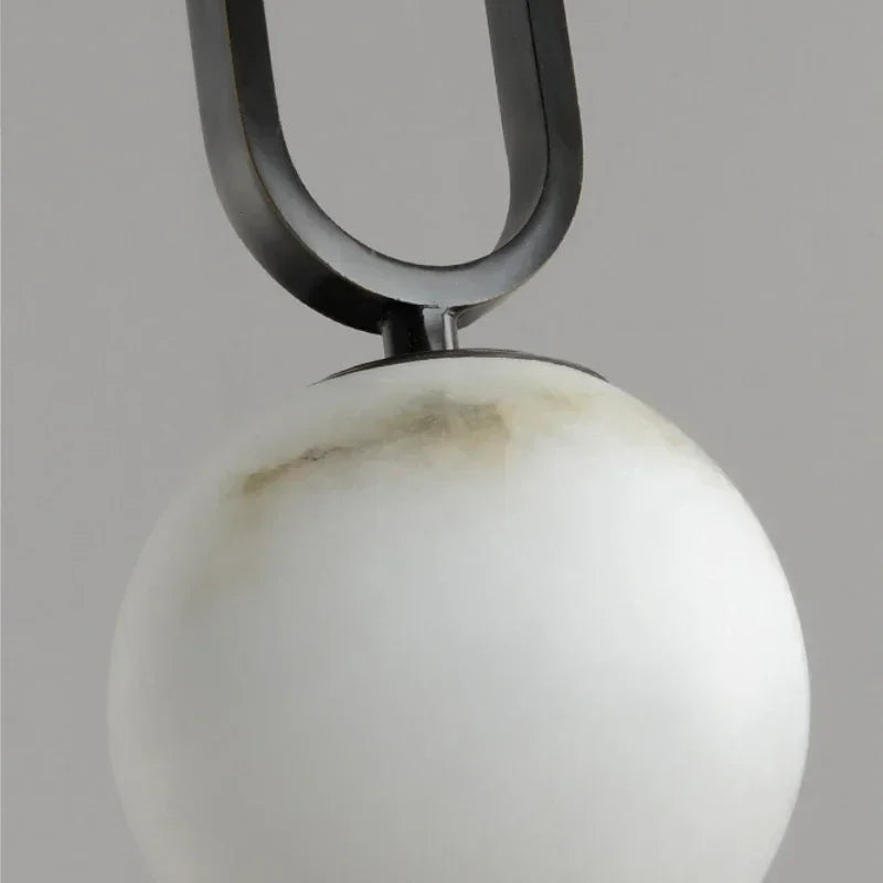 Close-up of a pendant with a white sphere and black U-shaped metal arm on a gray background