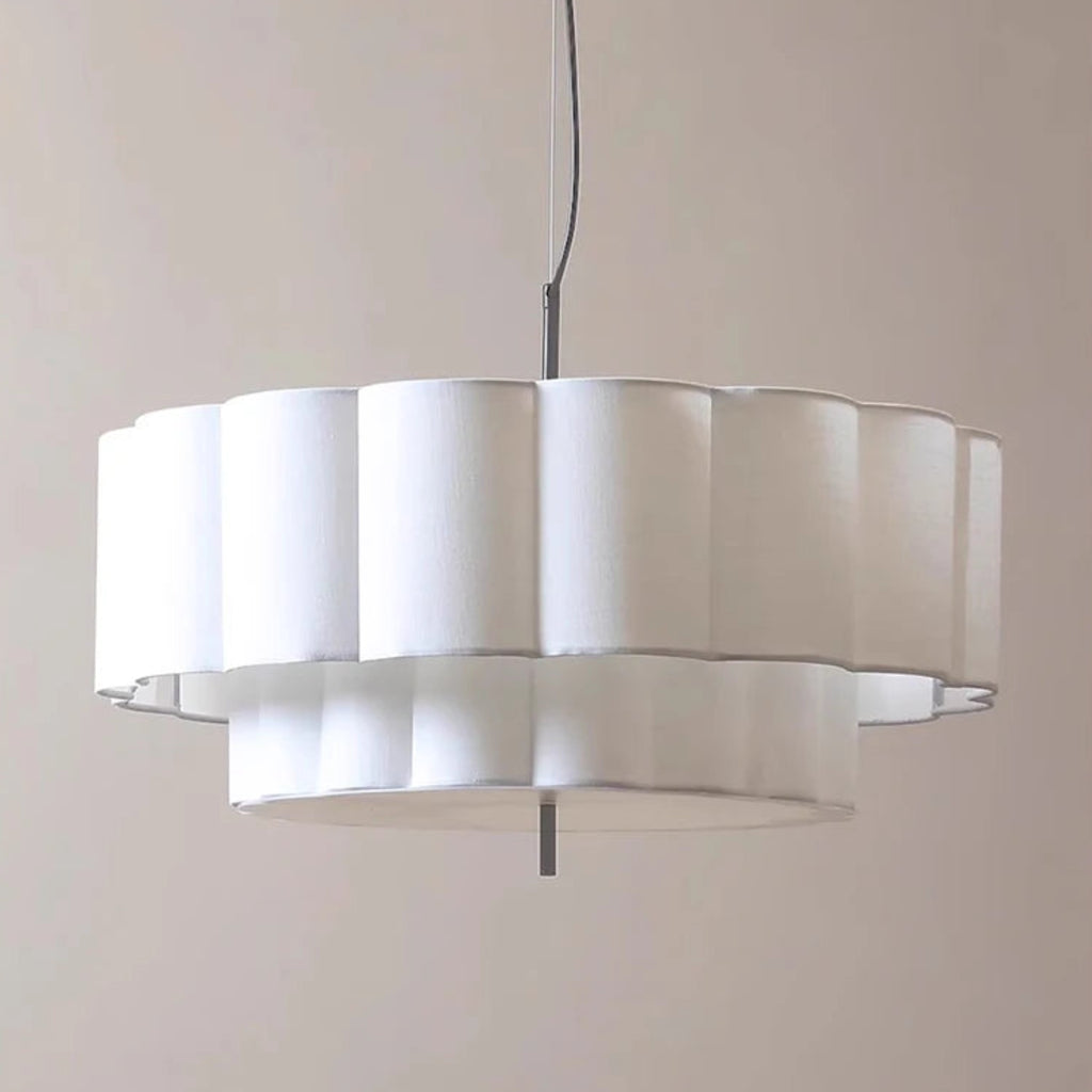 A modern white fluted pendant light with a tiered design, suspended by a thin black cord against a solid beige background.