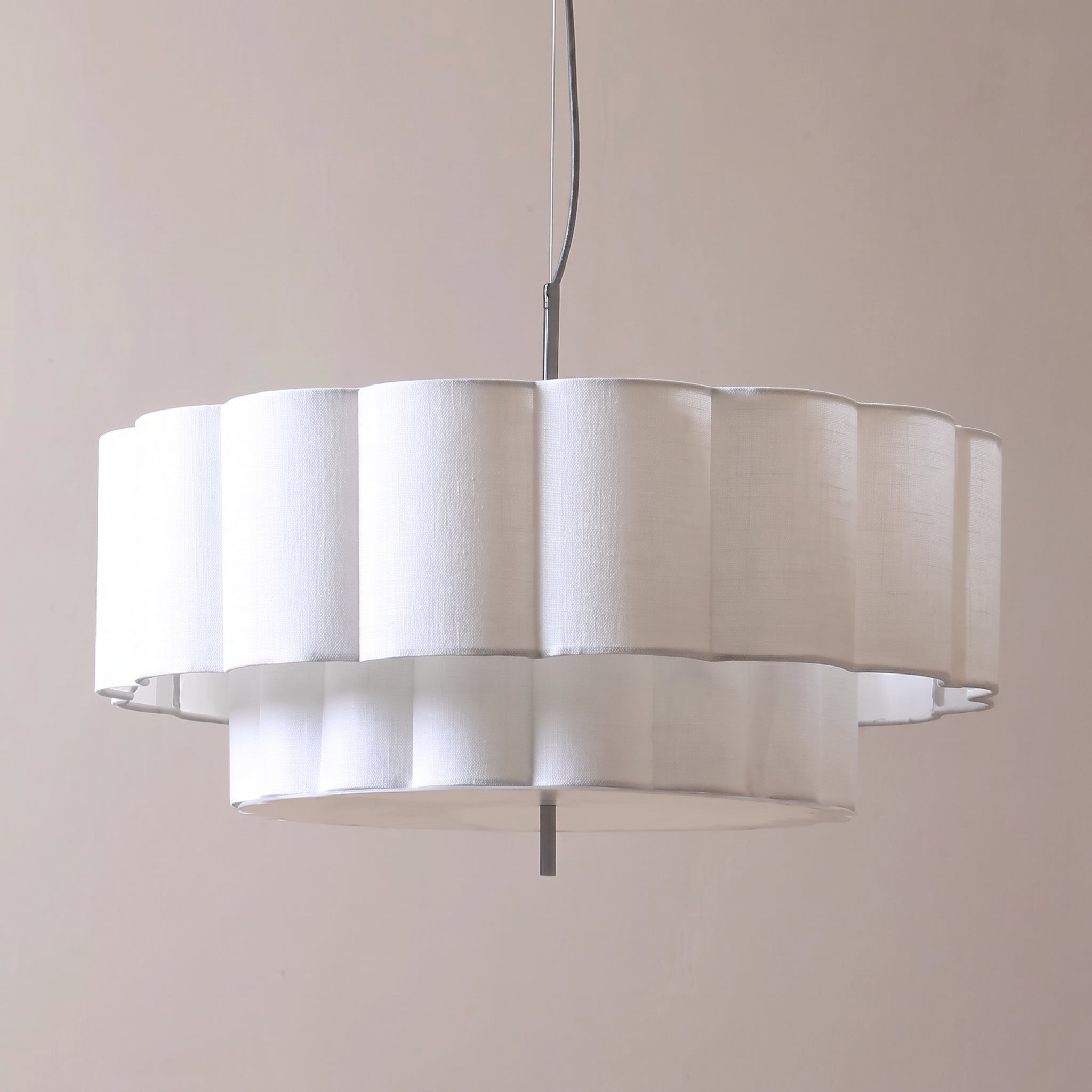 A modern circular pendant light with a white fluted fabric shade and a black hanging cord, shown against a plain beige wall.