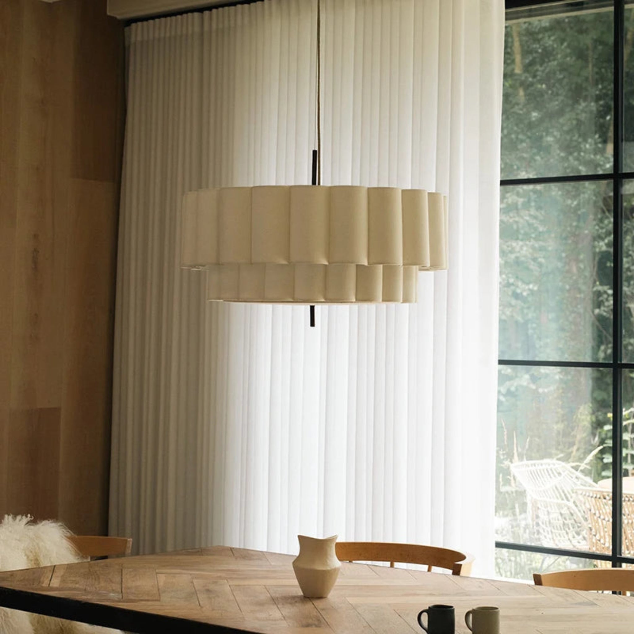 Beige pendant lamp hanging above a wooden table with a window in the background