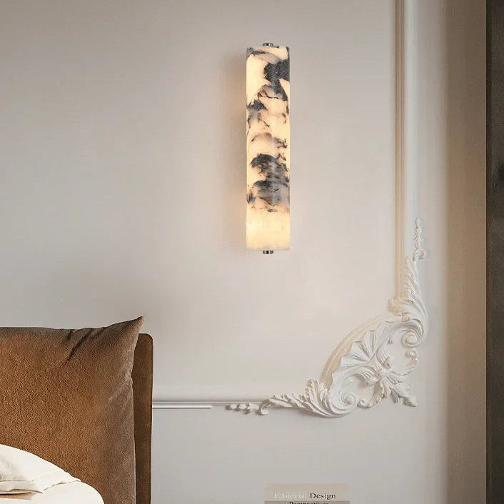 Wall-mounted light fixture in a bedroom setting with a bed and decorative box.