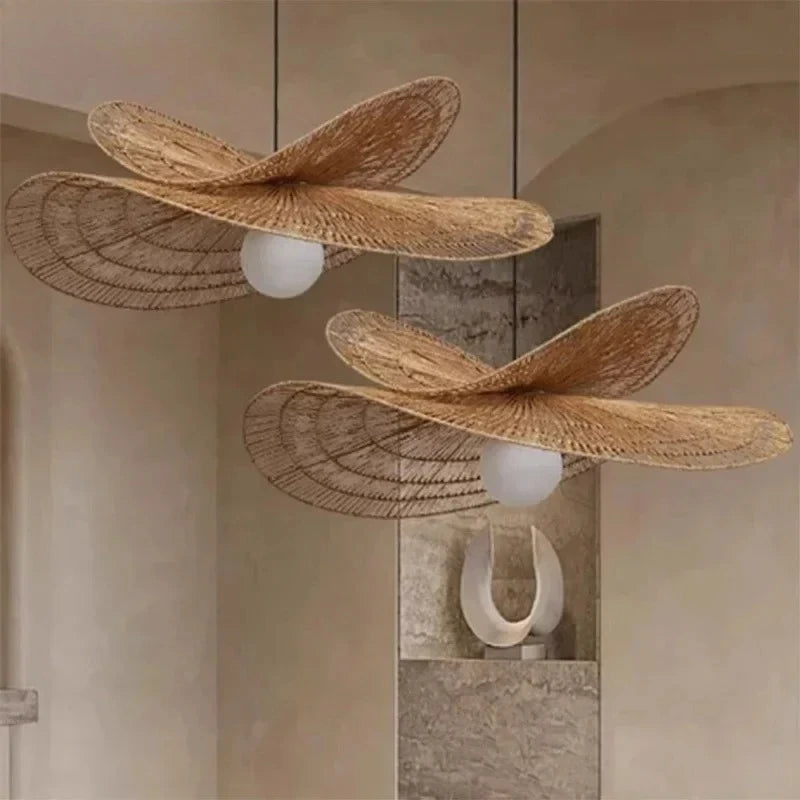 Two woven rattan pendant lights shaped like wings, suspended from black cords in a warm beige interior setting.