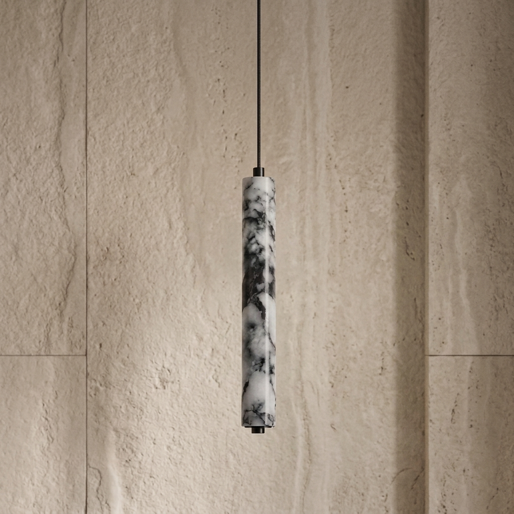 A modern pendant light with a cylindrical marble shade in black and white veining, suspended by a thin black cord against a textured beige stone wall.