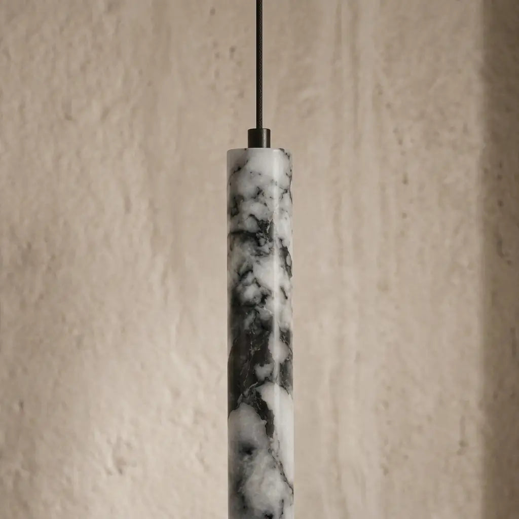 A modern pendant light with a cylindrical marble shade featuring black and white veining, suspended by a thin black cord against a textured beige wall.