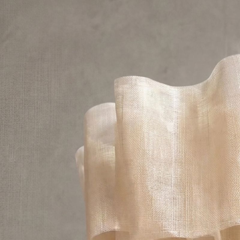 A cream-colored, ruffled fabric or paper wall sconce mounted on a textured gray wall.