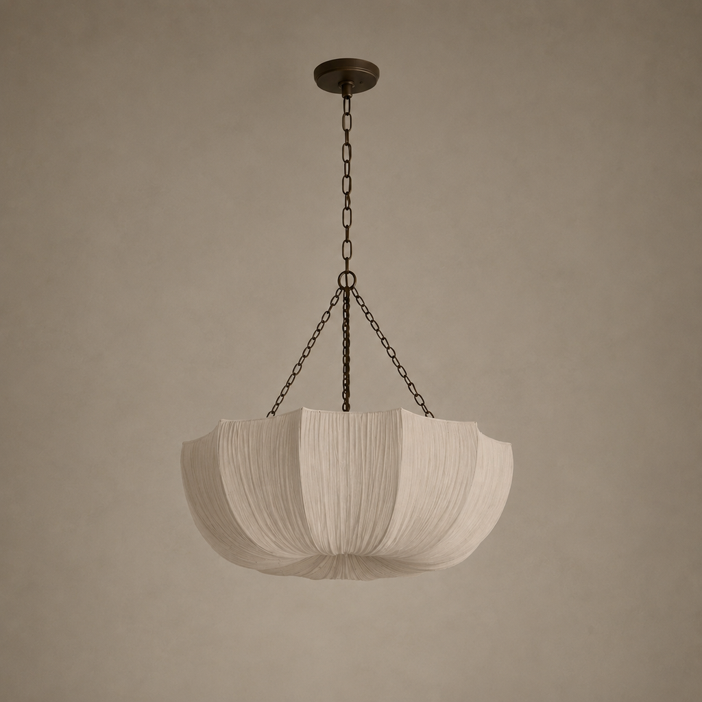 A modern pendant light with a pleated, lotus-shaped white fabric shade suspended by dark metal chains from a matching ceiling canopy, set against a warm, textured beige wall.