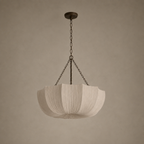 A modern pendant light with a pleated, lotus-shaped white fabric shade suspended by dark metal chains from a matching ceiling canopy, set against a warm, textured beige wall.