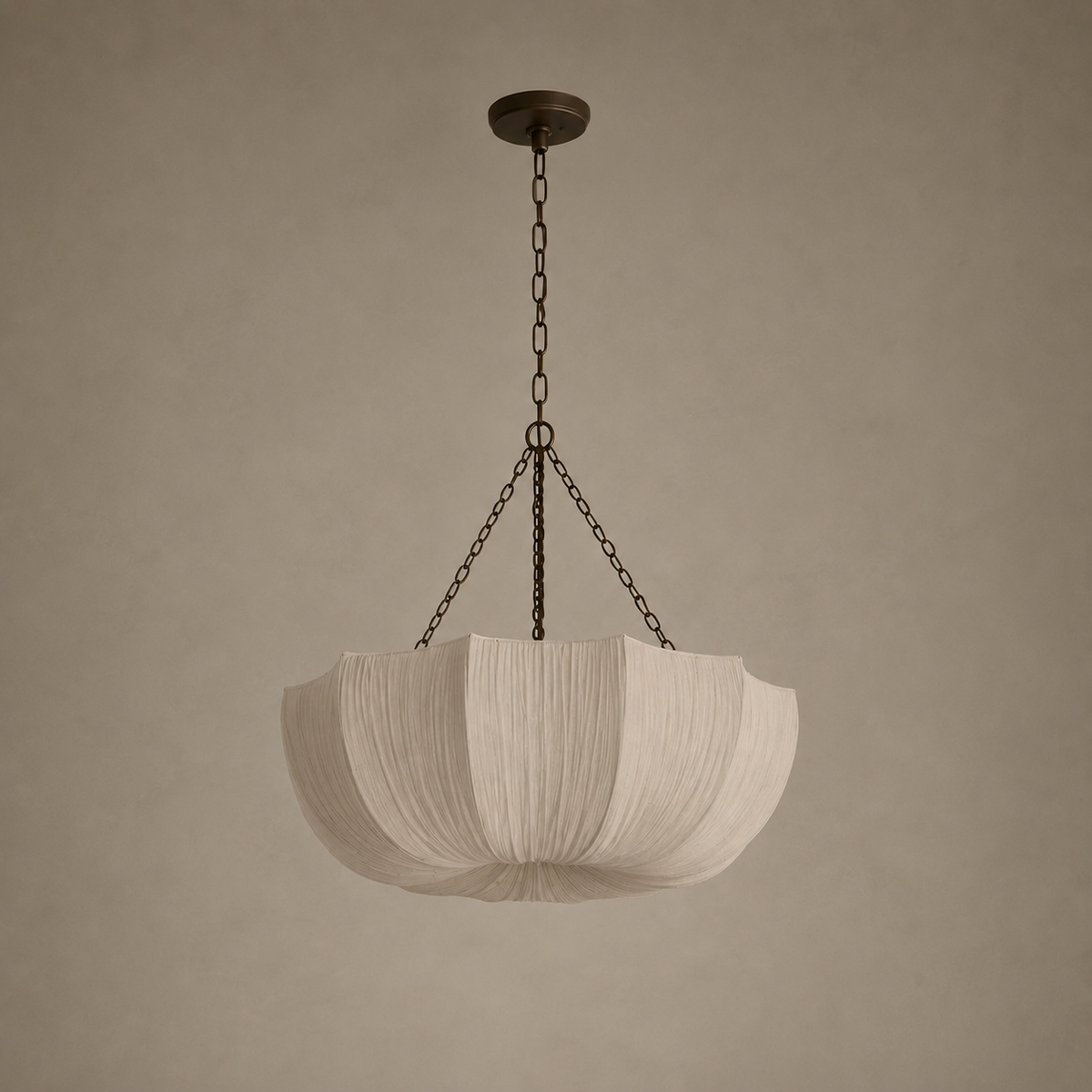 A modern pendant light with a pleated, lotus-shaped white fabric shade suspended by dark metal chains from a matching ceiling canopy, set against a warm, textured beige wall.