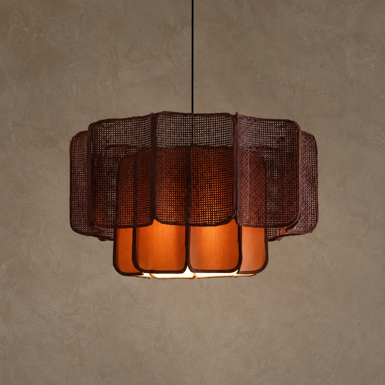 A modern pendant light fixture with a dark brown woven mesh outer shade and warm orange translucent inner panels, suspended against a textured beige wall.