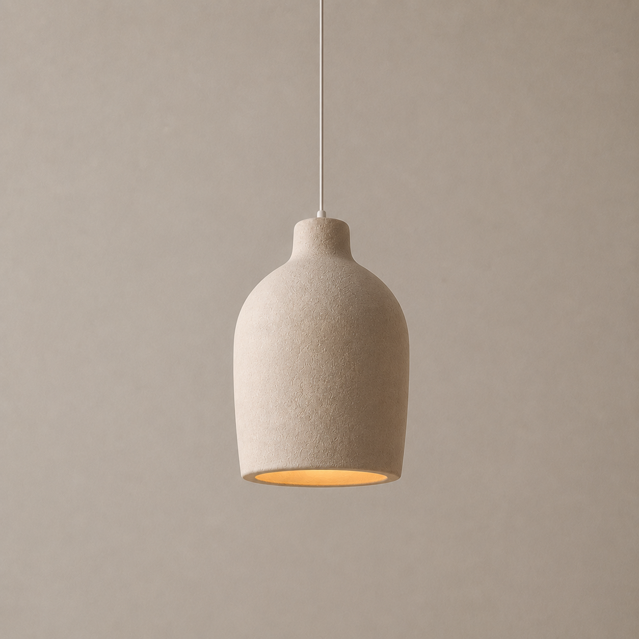 A modern pendant light with a textured, matte beige ceramic or stone-like shade, suspended by a thin white cord against a neutral, warm beige background.