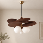 A modern pendant light fixture with five overlapping dark brown wooden shades and three white frosted glass globes, hanging from a black cord with a brass ceiling canopy in a neutral room.