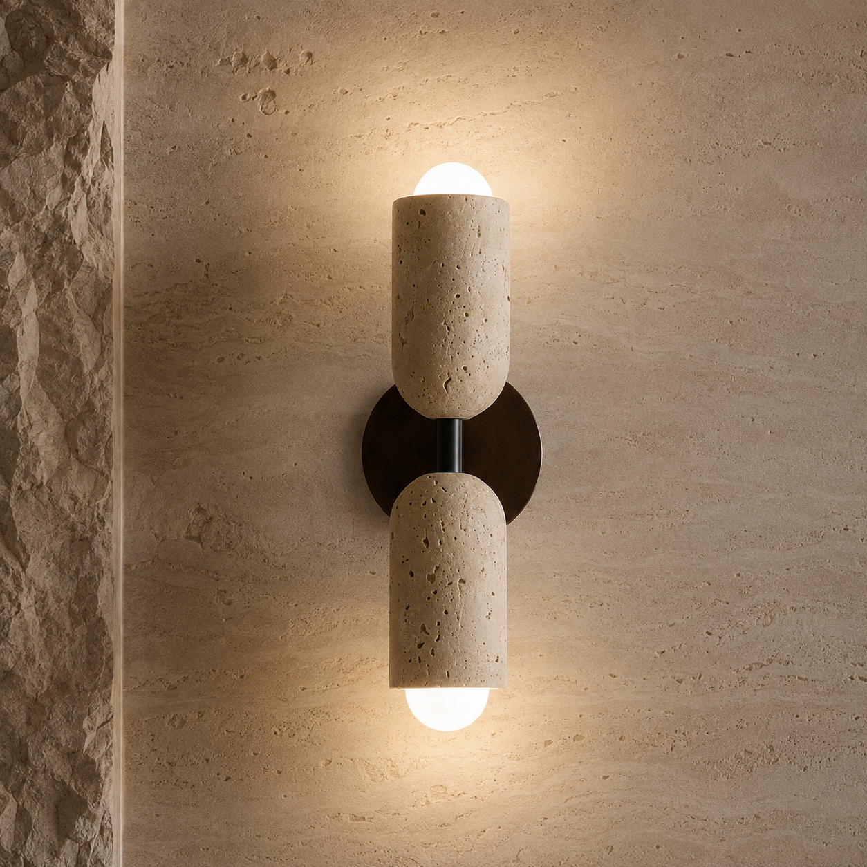 A modern two-light wall sconce mounted on a textured beige stone wall. The fixture features two cylindrical stone shades with a dark metal center and a glowing white frosted glass globe at the top and bottom.
