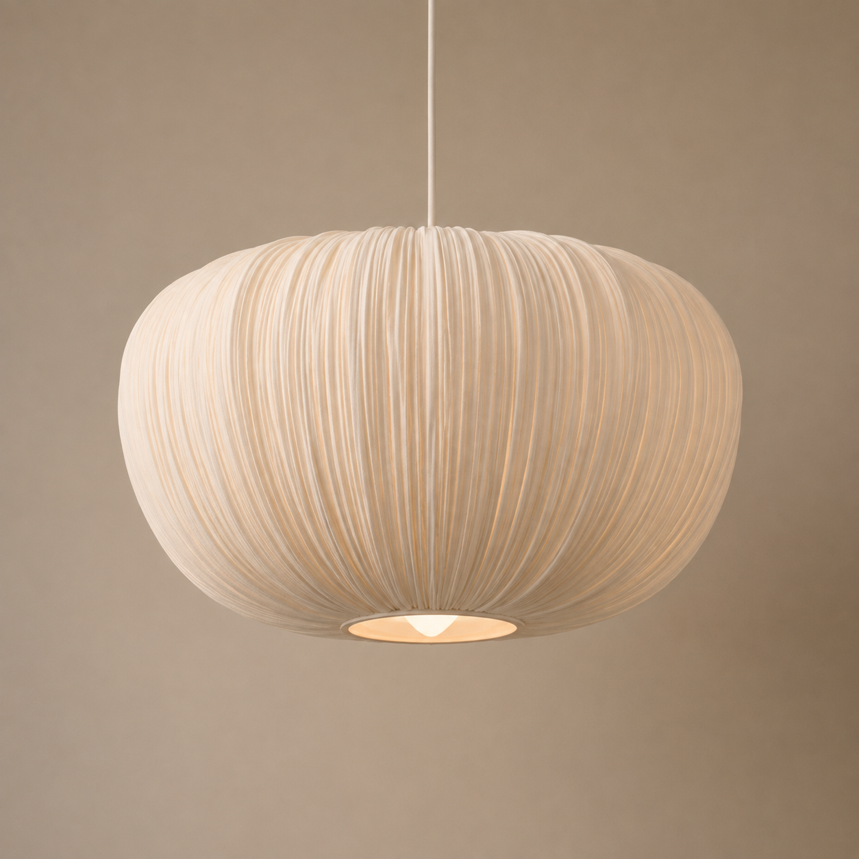 A modern pendant light with a pleated, ribbed fabric shade in a warm cream color, suspended by a thin white cord against a solid taupe background.