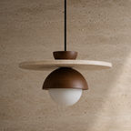 A modern pendant light with a dark brown metal dome shade, a white frosted glass globe bulb, and a round light beige stone disc shelf, suspended against a textured beige stone wall.