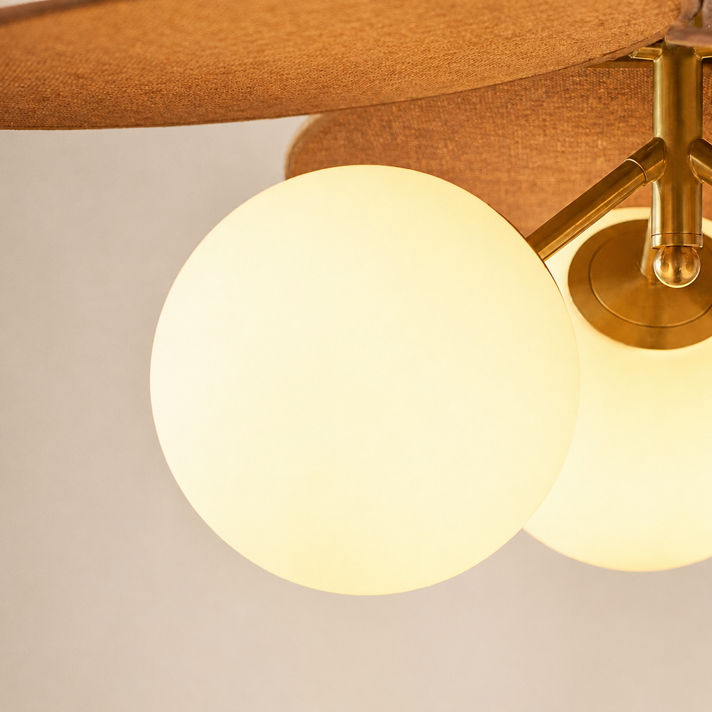 Close-up of a modern ceiling light fixture with two glowing frosted glass globe shades and a warm brass metal ceiling mount and canopy.