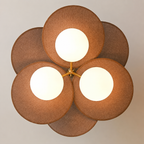 A modern five-light ceiling fixture with overlapping circular fabric shades in a warm brown tone and glowing white circular light centers, mounted on a neutral light gray wall.