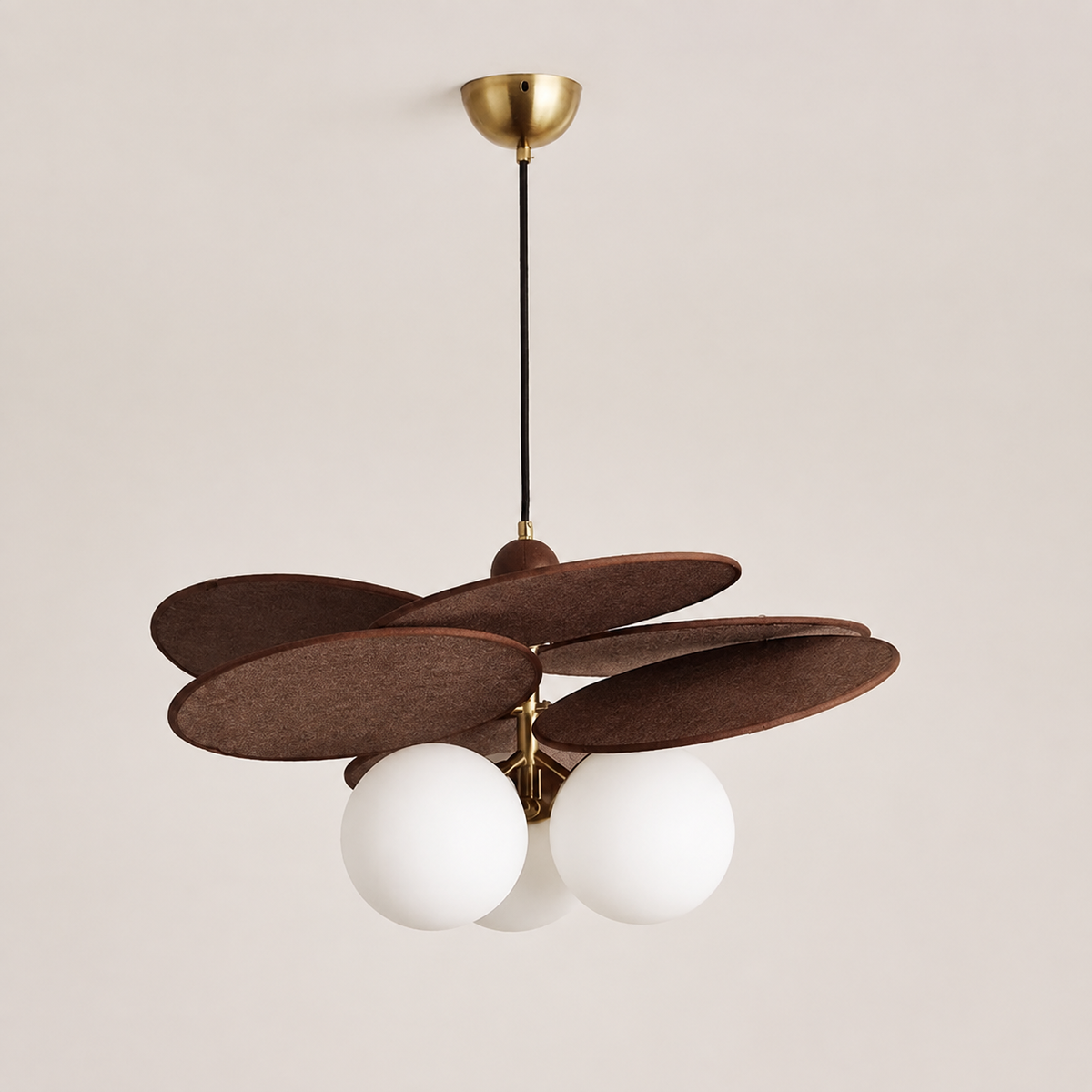 A modern three-light ceiling fixture with overlapping dark brown felt-like discs and three white spherical glass shades, suspended from a gold ceiling canopy by a black cord against a warm off-white wall.