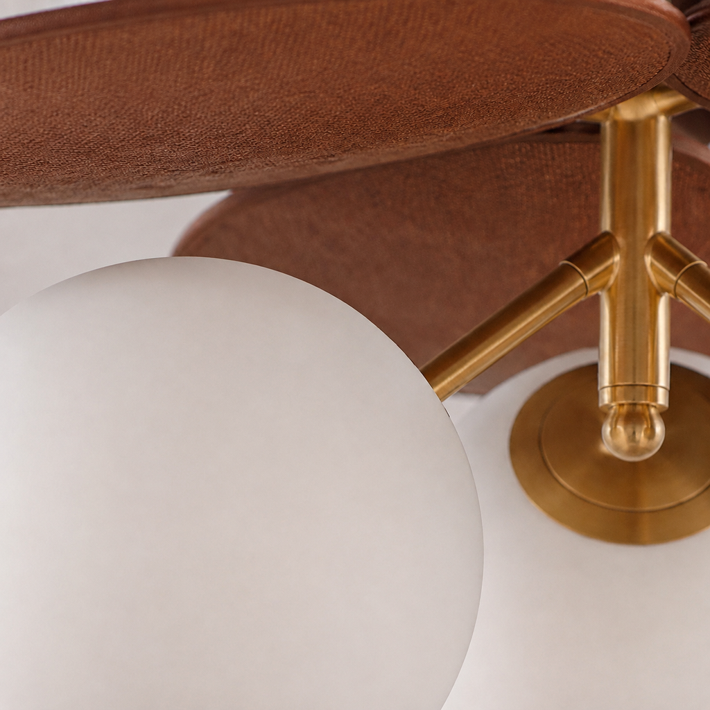 Close-up of a modern ceiling fan with a large white globe shade, a textured brown fabric canopy, and a polished brass metal hub and blades.