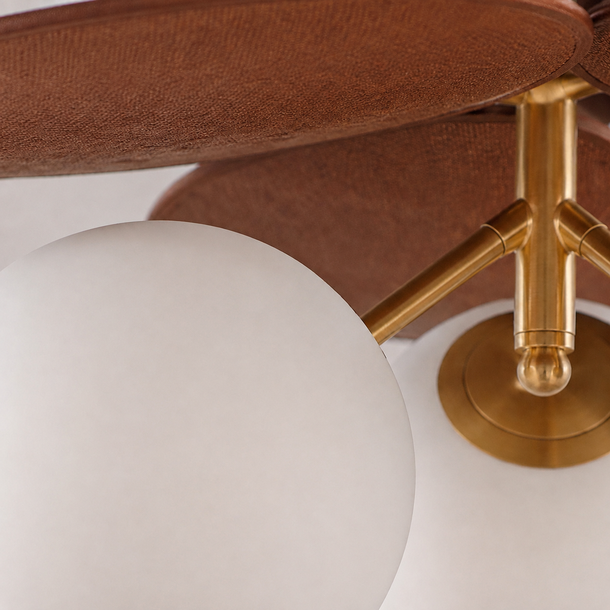 Close-up of a modern ceiling fan with a large white globe shade, a textured brown fabric canopy, and a polished brass metal hub and blades.