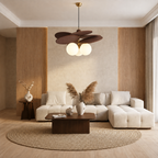 A modern living room featuring a cream tufted sectional sofa, a dark wood coffee table, a round jute rug, and a distinctive multi-leaf pendant light with glowing globe bulbs hanging above.