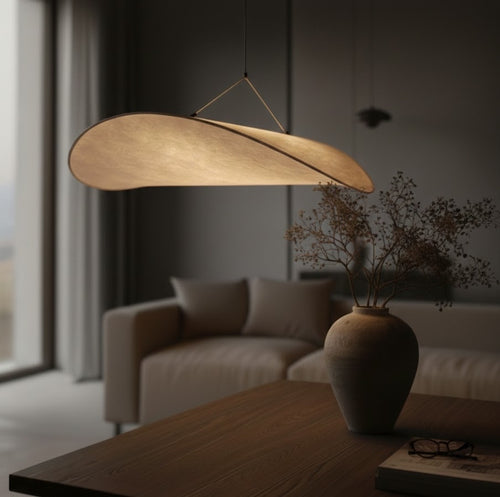 Modern pendant light hanging above a wooden table with a vase and glasses in a dimly lit room.